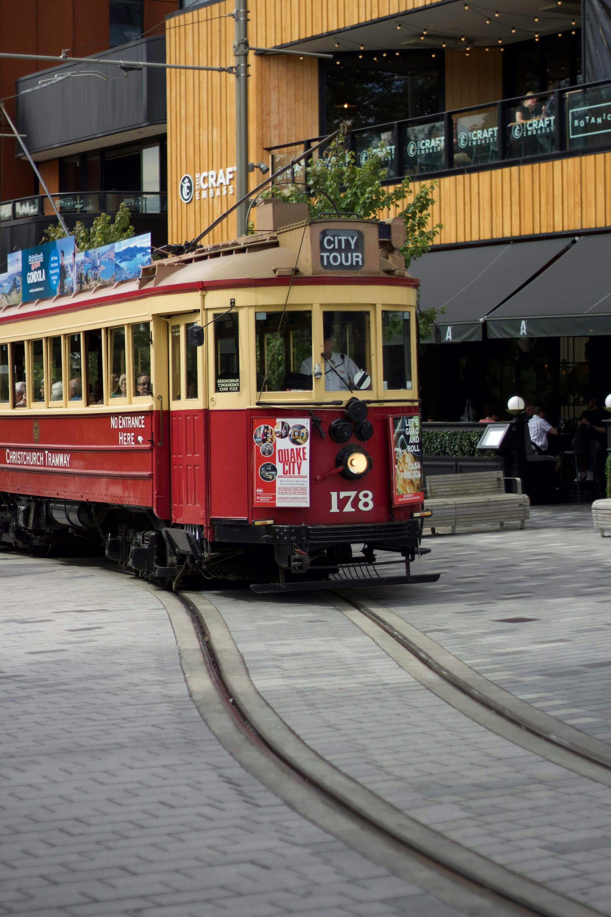 Red and white heritage tram running through central Christchurch on a clear day