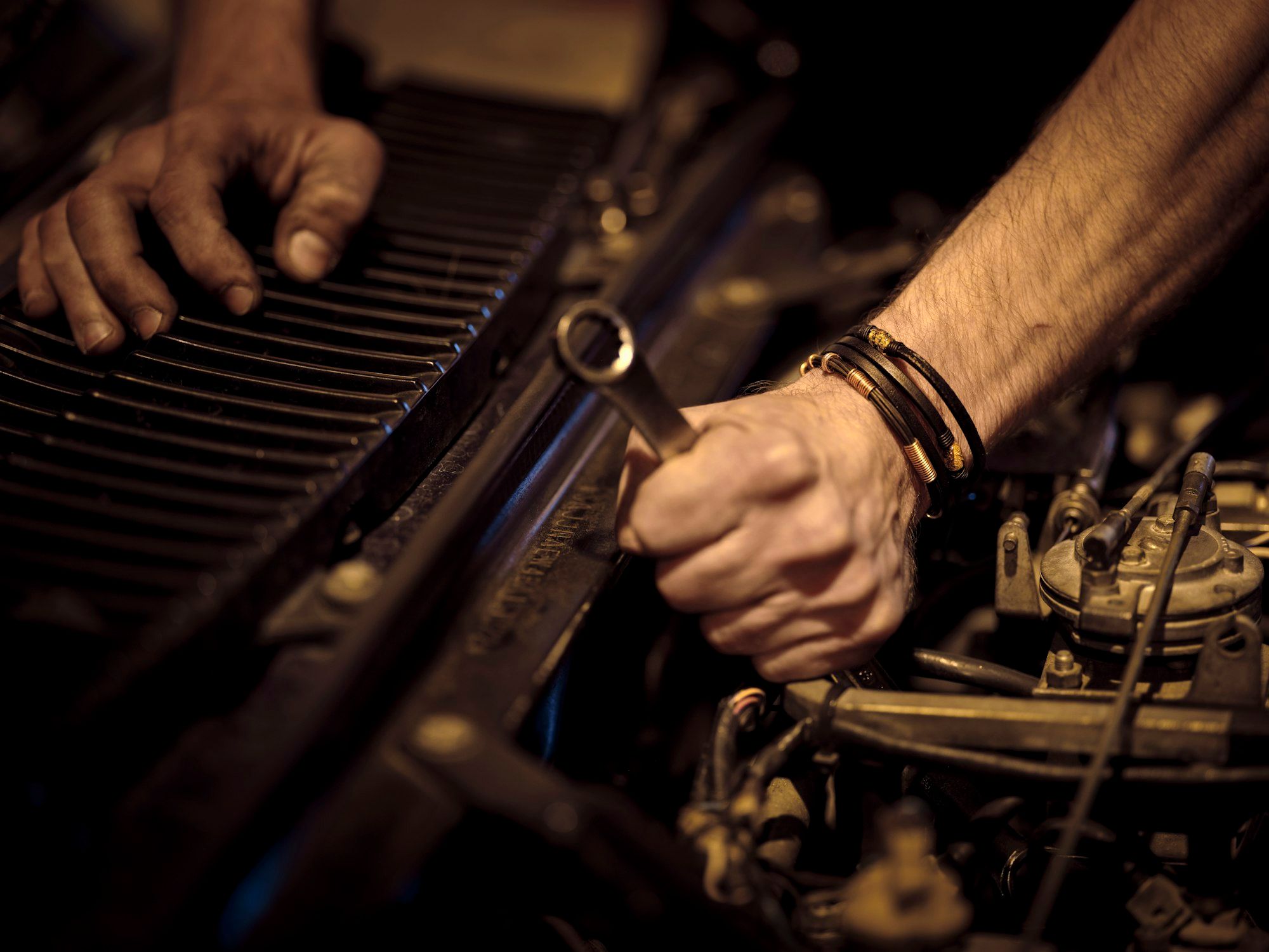 Mechanic's greasy hands working on a car engine with a spanner