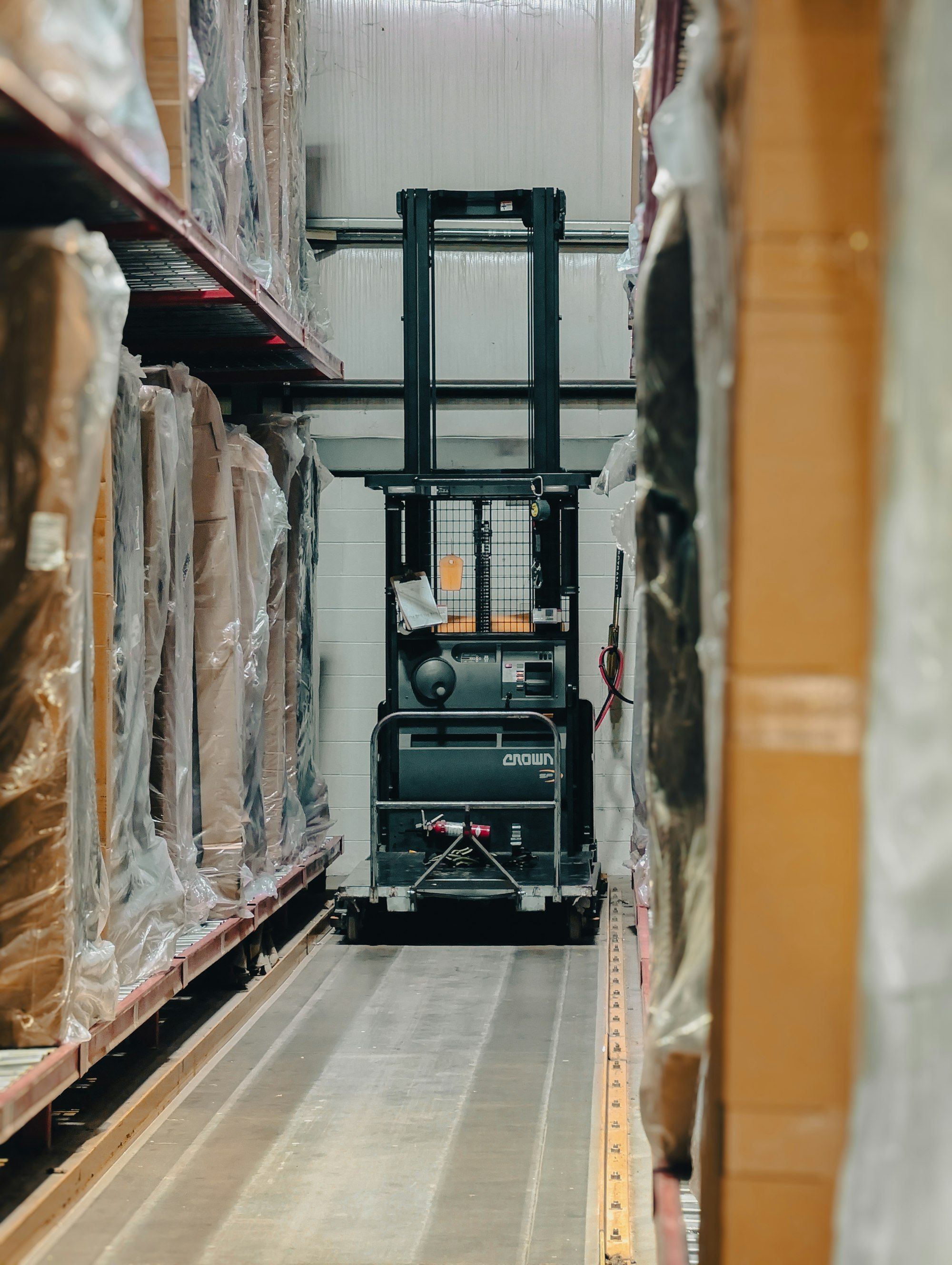 Forklift parked in a narrow warehouse aisle between tall racks of inventory